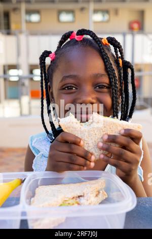 afroamerikanisches Schulmädchen am Tisch und gesundes Mittagessen mit Sandwich in der Grundschule Stockfoto