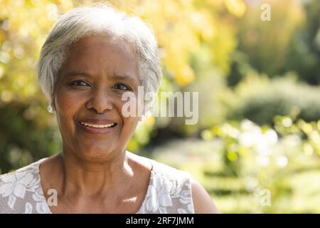 Porträt einer glücklichen älteren, birassischen Frau, die zu Hause im sonnigen Garten lächelt, Kopierraum Stockfoto