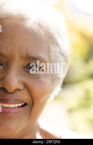 Ein halbes Porträt einer glücklichen älteren, birassischen Frau, die zu Hause im sonnigen Garten lächelt Stockfoto