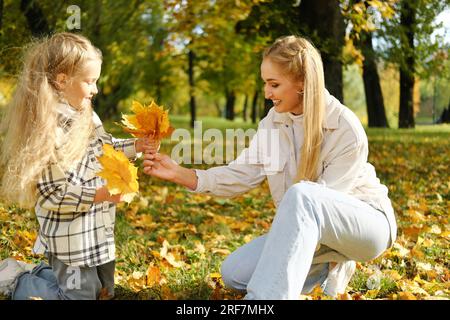 Familien verbringen Zeit zusammen im Herbstpark. Mutter und Tochter pflücken einen Strauß gelber Blätter. Horizontales Foto Stockfoto