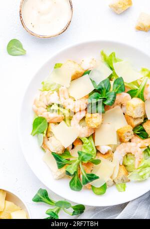 Gourmet-Caesar-Salat mit Garnelen, Eisberg und Salat, Croutons, Parmesan und caesar-Dressing. Weißer Tischhintergrund, Draufsicht Stockfoto