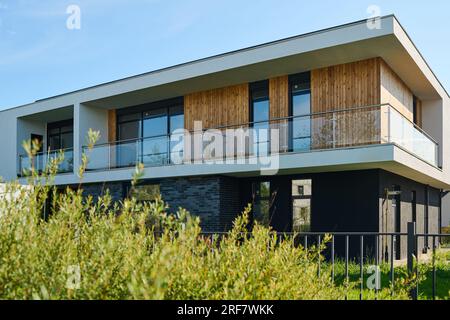 Seitenblick auf zweistöckiges Cottage mit Fenstergruppe und Balkon im zweiten Stock in ländlicher Umgebung Stockfoto