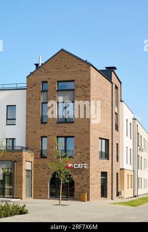 Ecke eines großen 3-stöckigen Wohnblocks mit einem kleinen Cafe im vorderen Teil, das in der zentralen Straße der Stadt oder in ländlicher Umgebung steht Stockfoto