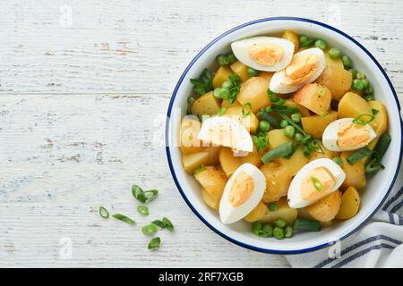 Traditioneller Kartoffelsalat mit Speck und Eiern in einer weißen Schüssel. Picknick-Food-Konzept. Schüssel mit warmem Kartoffelsalat. Deutscher Kartoffelsalat. Draufsicht. Stockfoto