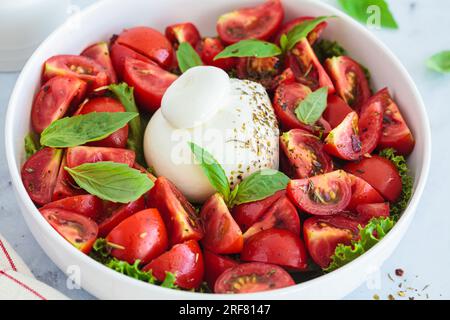 Burrata-Salat mit Tomaten und Basilikum auf einem weißen Teller, Nahaufnahme. Stockfoto