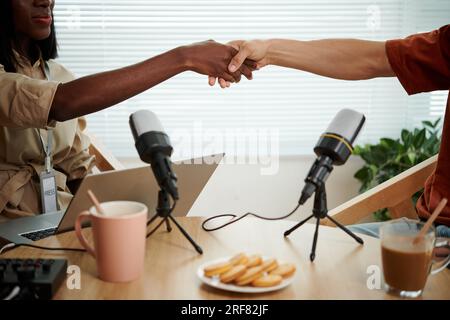 Zugeschnittenes Bild von Podcaster und Gast, der die Hände über den Tisch schüttelt Stockfoto