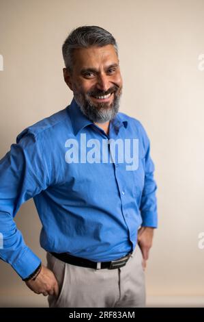 Selbstbewusster leitender Vorgesetzter, der vor die Kamera schaut und den beigen Hintergrund lächelt Stockfoto