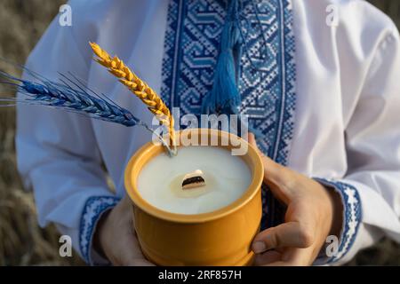 Kerze in der Hand eines Kindes in einem bestickten ukrainischen Hemd und zwei Stacheln in gelb-blauen Farben der ukrainischen Flagge. Stacheln und Feuer im Gedächtnis Stockfoto