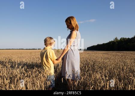 Mutter und Sohn, die Händchen halten, stehen auf einem Weizenfeld zwischen Stacheln. Genießen Sie Natur und Leben, Zusammensein. Tag Der Erde. Stoppt den Krieg in der Ukraine. Zurück Stockfoto