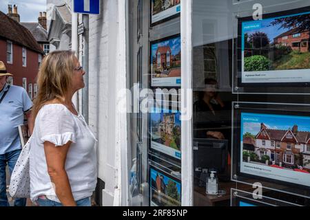 Eine Frau schaut sich Immobilien zum Verkauf an, im Fenster eines Immobilienmaklers, High Street, Lewes, East Sussex, Großbritannien. Stockfoto