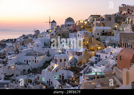 Häuser, Villen und Windmühlen an den Klippen im Dorf Oia (Ia) bei Einbruch der Dunkelheit, Santorin, Griechenland Stockfoto