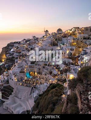 Häuser, Villen und Windmühlen an den Klippen im Dorf Oia (Ia) bei Einbruch der Dunkelheit, Santorin, Griechenland Stockfoto