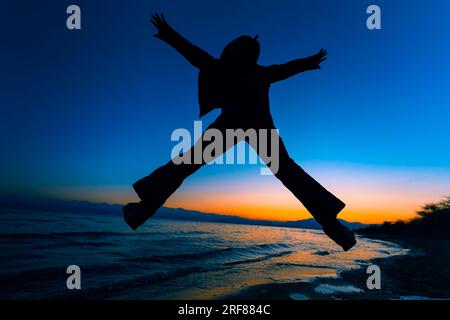 Ein Mann, der bei Sonnenuntergang auf die Silhouette des Sees springt Stockfoto
