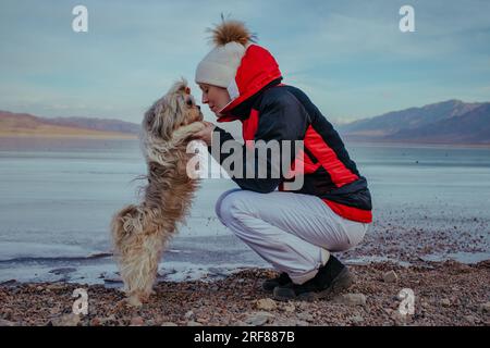 Junge Touristin mit Hund, der im Winter auf einem gefrorenen See posiert Stockfoto