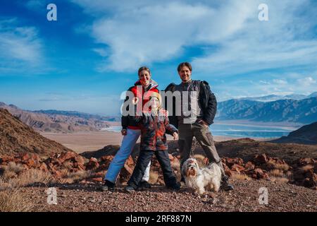 Vater, Mutter, Sohn und Hund, glückliche Familie, die im Winter im Hintergrund in den Bergen posiert Stockfoto