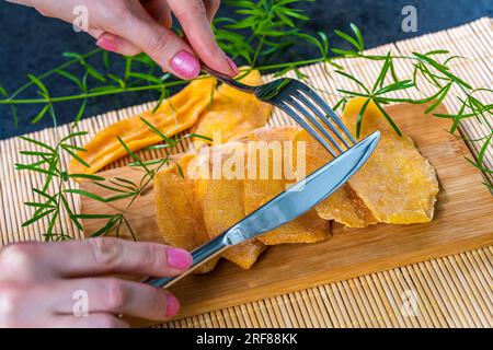 Küchentisch mit getrockneter Mango an Bord, Frau mit Gabel und Messer Stockfoto