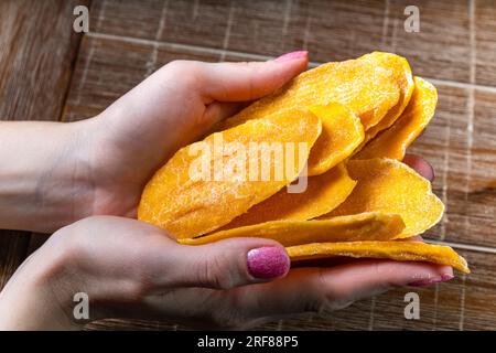 Junge Frau, die getrocknete Mango auf Tischhintergrund in den Händen hält Stockfoto