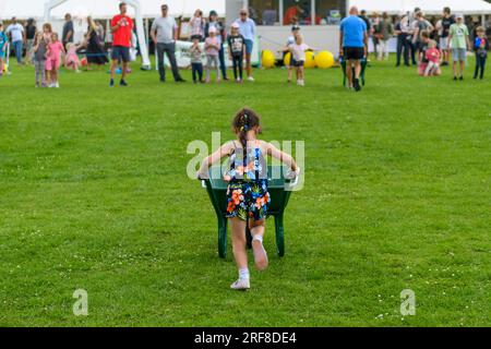 Ein Mädchen schiebt eine Schubkarre während eines Schubkarren-Rennens auf einer Landmesse. Damerham, Hampshire, Großbritannien, August 2023 Stockfoto