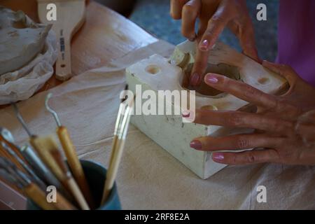 Nahaufnahme von Frauenhänden, die mit Ton arbeiten, Töpferwaren herstellen, professionelle Keramikkünstlerin, die manuellen Baukurs in einer modernen Töpferwerkstatt gibt Stockfoto