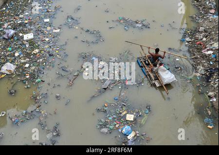 27. Juli 2023 Sylhet-Bangladesch: Ein Vater und sein Sohn rudern zusammen auf einem handgefertigten Floß und suchen nach Recyclingprodukten aus Plastikabfällen, die zum Verkauf aus dem mit Plastikabfällen gefüllten Kanal von Kazir Bazar in Sylhet bestimmt sind. Dieser Kanal ist direkt mit dem Surma-Fluss Sylhet, Bangladesch verbunden, der den Surma-Fluss verschmutzt und das Flussbett füllt. Das Polyethylen hat sich in riesigen Haufen Schlamm angesammelt, was die Navigation behindert und zu einem Mangel an nutzbarem Wasser aus dem Surma-Fluss von Bangladesch führt. Am 27. Juli 2023 Sylhet, Bangladesch (Foto: MD Rafayat Haque Khan/Eyepix Group/Sipa USA) Stockfoto