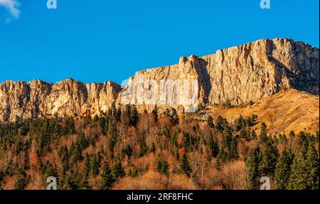 Steile Klippen mit flachen Spitzen am Fuß bedeckt mit herrlichen dichten Herbstwäldern Stockfoto