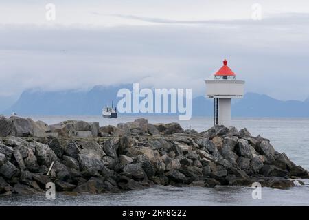 Kleiner Leuchtturm, am Ende einer Kaimauer, und die Fähre nach Gryllefjord, von einem Boot aus gesehen. Andenes, Andøya, Vesterålen-Archipel, Nordland, Norwegen Stockfoto