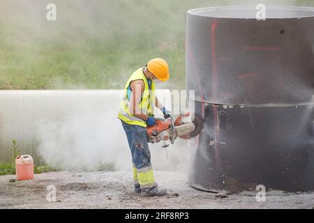 Installation eines Betonrohrs im Boden zum Auffangen von Regenwasser. Der Arbeiter schneidet Löcher in den Betonteil des Rohrs, um ihn mit dem Regenabfluss zu verbinden. A Stockfoto