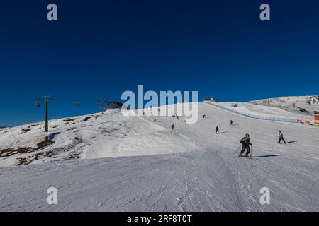 Falcade, Italien - 15. Februar 2023: Skipiste mit Skifahrer unter blauem Himmel. Die Leute fahren die schneebedeckten Berge auf Skiern hinunter. Eine Gruppe von Skifahrern auf einer Skipiste Stockfoto