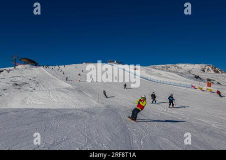 Falcade, Italien - 15. Februar 2023: Skipiste mit Skifahrer unter blauem Himmel. Die Leute fahren die schneebedeckten Berge auf Skiern hinunter. Eine Gruppe von Skifahrern auf einer Skipiste Stockfoto