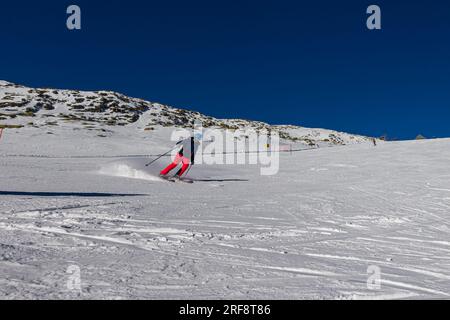 Falcade, Italien - 15. Februar 2023: Skipiste mit Skifahrer unter blauem Himmel. Die Leute fahren die schneebedeckten Berge auf Skiern hinunter. Eine Gruppe von Skifahrern auf einer Skipiste Stockfoto