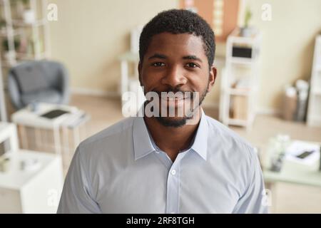 Nahaufnahme von vorne, ein lächelnder schwarzer Mann, der im Büro steht und in die Kamera schaut Stockfoto