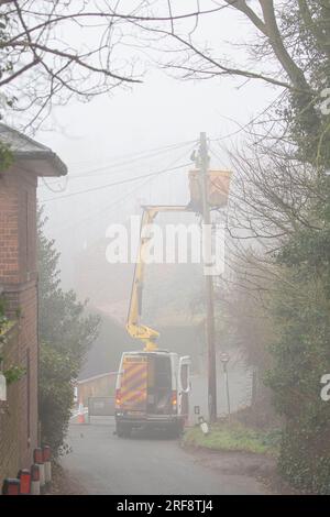 Telecom Engineer in einem Van Cherry Picker Lift, der an einem nebligen Tag auf einer britischen Landstraße an einem Telegrafenmast arbeitet. Stockfoto