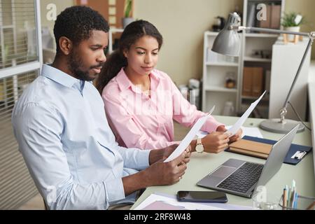Porträt zweier afroamerikanischer Männer und Frauen, die Dokumente diskutieren, während sie am Schreibtisch im Büro sitzen Stockfoto