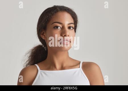 Nahaufnahme eines jungen afroamerikanischen Mädchens, das vor der Kamera schaut, vor weißer, einfacher Schönheit Stockfoto