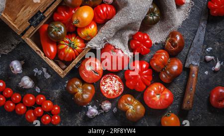 Viele verschiedene Arten, Formen und Größen von Tomaten in einer alten Holzkiste und auf einer dunklen Oberfläche, flach liegend, Draufsicht. Erntekonzept Stockfoto