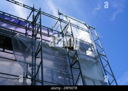 Abstrakter röhrenförmiger modularer Metallgerüstbau mit Sicherheitsnetz um die Fassade des Hauses auf blauem Himmelshintergrund Stockfoto