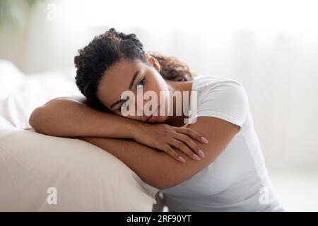 Porträt Einer Aufgewühlten Schwarzen Frau, Die Sich Im Schlafzimmer Zu Hause Auf Das Bett Lehnt Stockfoto