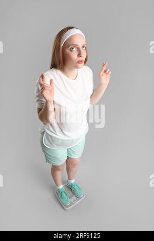 Besorgte junge Frau, die ihr Gewicht auf einer Waage vor grauem Hintergrund misst Stockfoto