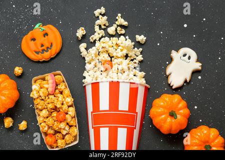 Zusammensetzung mit leckerem Popcorn, Keksen und Kürbissen auf dunklem Hintergrund. Halloween-Feier Stockfoto