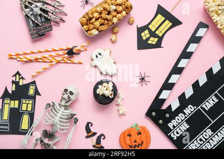 Zusammensetzung mit leckerem Popcorn, Skelett und Klapperbrett auf pinkfarbenem Hintergrund. Halloween-Feier Stockfoto