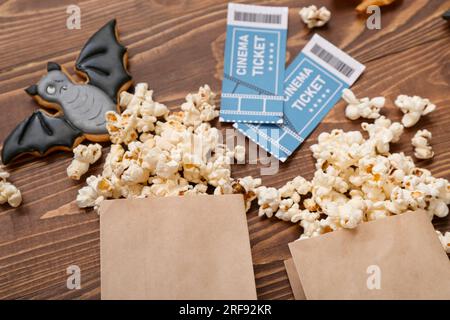 Papiertüten mit leckerem Popcorn, Keksen und Kinokarten auf Holzhintergrund, Nahaufnahme. Halloween-Feier Stockfoto