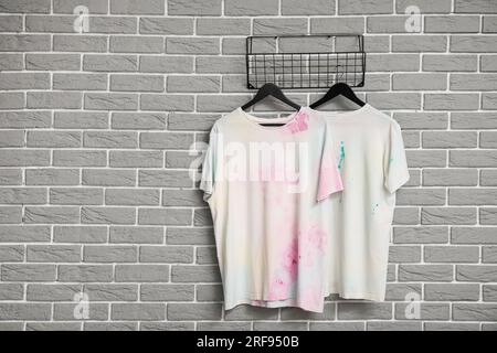 Elegante weiße T-Shirts, die an grauen Ziegelwänden hängen Stockfoto