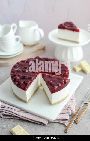 Gebackene weiße Schokolade und Kirschkäsekuchen auf einem weißen Teller. Weiße Kaffeetassen und rosafarbener Hintergrund. Stockfoto