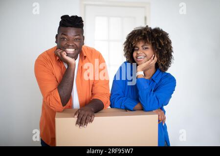 Immobilien. Fröhliches Schwarzes Paar, Das Am Umzugstag Mit Einer Pappkiste Posiert Stockfoto