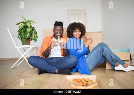 Mittagspause. Happy Black Ehegatten Essen Pizza Und Feiern Den Umzug Ins Neue Zuhause Stockfoto