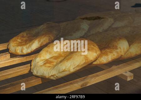 Frisch gebackenes Pita-Brot liegt auf einem Holzständer in einer Bäckerei. Blick von der Straße durch ein Glasfenster. Stockfoto