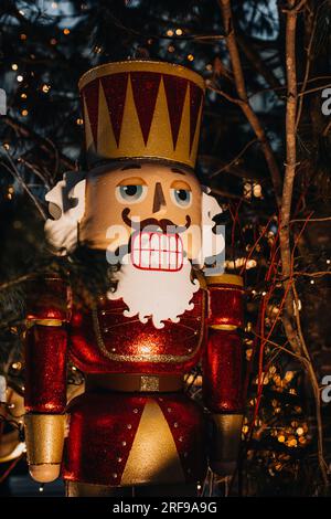 Weihnachtsspielzeug, riesiger Nussknacker aus Holz mit Girlandeleuchten am Abend. Festliche Einrichtung, Silvester-Winter-Details im Freien. Vertikal Stockfoto