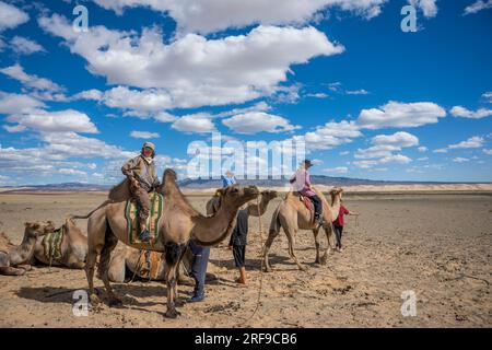 Touristen auf einem Bactrianischen Kamelritt in einem Kamelhirtenlager in der Nähe der Sanddünen Hongoryn Els in der Wüste Gobi in der südlichen Mongolei. Stockfoto