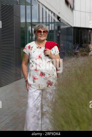 Eine Wirklich Moderne Seniorin Mit Sonnenbrille Geht In Der Nähe Des Einkaufszentrums Spazieren. Portrait Von Happy Senioren Female, Genießt Pensionierung Leben In Der Stadt. Authentisch Stockfoto