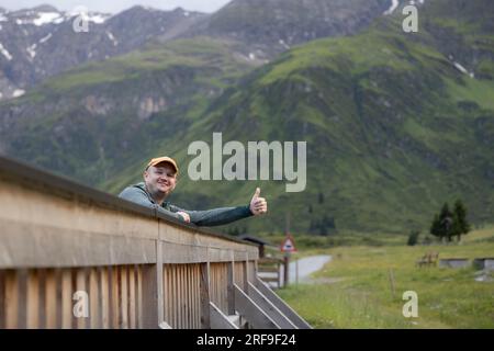 Ein junger Mann steht auf einer hölzernen Brücke mit großer Laune im Alpental des Sportgasteins, Österreich Stockfoto